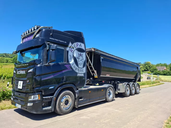 Schwarzer Scania Sattelzug der Riepa Logistic GmbH mit Kippmulde auf einer Straße zwischen Weinbergen in der Südpfalz