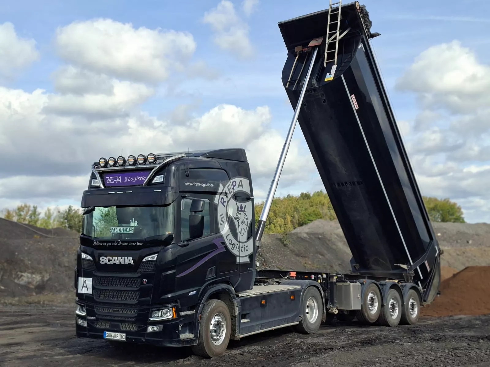 Schwarze Scania Sattelzugmaschine der Riepa Logistic GmbH mit angehobener Kippmulde beim Abkippen von Material
